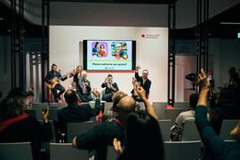 Picture of the International Stage: The speakers on stage and the audience in the public of the live The Hof Event raise their glasses.