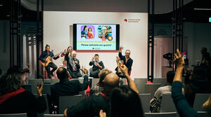 Picture of the International Stage: The speakers on stage and the audience in the public of the live The Hof Event raise their glasses.