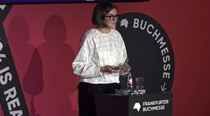 A woman stands at a lectern and speaks to the audience.