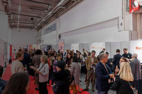 Menschen stehen bei einem Networking-Empfang in einer Messehalle zusammen und unterhalten sich. 